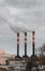 Three factory chimneys release clouds of smoke into the sky.