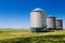 Three farm grain silos for agriculture. New and old silos. Placed next to the cultivated field. Countryside in south america.