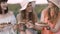 Three female friends, sitting on the blanket in meadow and holding wooden plates with escargots