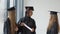 Three female students of different races with a diploma in their hands. Graduates in black robes and square hats have a