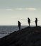 Three Fisherman silhouettes on the top of a seawall, at Esposende beach, Braga, Portugal.