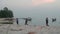 Three fishermen walk along the shore against the backdrop of the sea and boats.