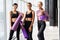 Three fitness young girls in sportswear standing against wall in fitness gym. Girls smiling and looking to the camera