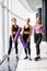 Three fitness young girls in sportswear standing against wall in fitness gym. Girls smiling and looking to the camera