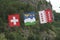 Three flags of Switzerland, Wallis and Val d`HÃ©rens next to each other in front of a mountain and trees