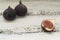 Three fresh figs on a wooden white table. One fig is cut in halves and its flesh is visible. Located in a group.