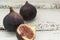 Three fresh figs on a wooden white table. One fig is cut in halves and its flesh is visible. Located in a group