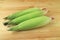 Three fresh purple corns with bright green husks and silks isolated on wooden background