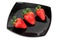 Three fresh strawberries on black saucer