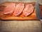 Three fresh uncooked raw port chops on a wooden cutting board. Simple white table cloth