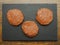 Three fresh uncooked turkey burgers on a black slate plate.