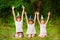 Three friendly children in festive cone caps, sit on grass, have fun together as celebrate birthday