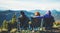 Three friends sit in camping chairs on top of a mountain, travelers enjoy nature and cuddle, tourists look into distance on back