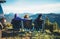 Three friends sit in camping chairs on top of a mountain, travelers enjoy nature and cuddle, tourists look into distance on back