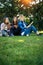 Three friends spend their free time sitting in the park on green lawn. Young pretty girls talking, smiling, looking photo