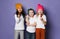 Three funny kids friends in white t-shirts and colorful hats stopped their play to eat enjoy candies on purple