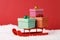 Three gift boxes with bow on red sled on snow on red background