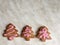 three ginger herringbone-shaped cookies, with pink icing sugar on a grey background