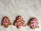 three ginger herringbone-shaped cookies, with pink icing sugar, grey background. ginger biscuits in herringbone form with pink