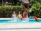 Three girls from different ethnic groups with bathing suits of different colors splashing the water of a swimming pool and with a