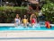 Three girls from different ethnic groups with bathing suits of different colors splashing the water of a swimming pool and with a