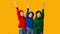 Three Girls Gesturing Victory Sign Raising Hands Standing, Yellow Background