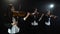 Three girls in play the violins in a composition in a room. Black background