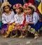 Three girls in traditional Ecuadorian clothes sit on street curb