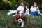 Three girls, wearing white shirts and blue jeans, sitting on grass, playing with small dog in park. Cavalier king charles spaniel