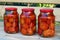 Three glass cans of red tomatoes on the wooden bench