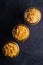 Three glass jars in row with variety of uncooked golden wheat pasta on dark black textured background