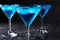 Three glasses of blue cold martini cocktail with ice and clear dew drops on glass on a gray background , closeup shot