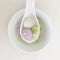 Three glutinous rice balls of different flavors and colors scooped up from a white bowl on a white spoon. minimalist, square.