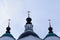 Three golden crosses of a white stone orthodox chirch with black dark domes against a blue cloudy background