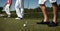 Three golf players on green field.