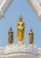 Three graceful and peaceful golden Buddha statues standing under beautiful white arch with blue sky background