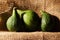 THREE GREEN FIGS ON A SHELF ON A PIECE OF HESSIAN