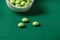 Three green vitamins on table against the background of jar of pills.