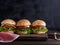 Three hamburgers with vegetables on a brown wooden board