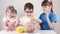 Three happy children take out marshmallows from jar and eat on table