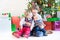 Three happy children - teenager boy, toddler girl and their newborn baby brother - playing together under Christmas tree