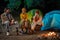 Three happy friends enjoying camping with tent chatting by a fire having fun together in nature