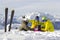 Three happy friends snowboarders and skier are having lunchtime on ski slope in sunny day in the mountains