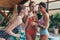 Three happy girlfriends in swimwear drinking juice from bottles at swimming pool in spa center