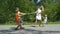 Three happy kids playing tug-of-war in city park with mum.