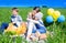 Three happy kids sitting on picnic on the field. blue sky, green grass. bread, pies and fruits in a basket.