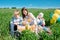 Three happy kids sitting on picnic on the field. blue sky, green grass. bread, pies and fruits in a basket.