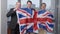 Three happy men and woman holding British flag in office looking at camera smiling and jumping. Positive successful