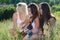 Three happy teen girls singing and playing guitar on green grass