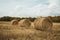 Three haystacks on wheat crop field against dramatic cloudy blue sky. Wheat yellow golden harvest in summer. Countryside